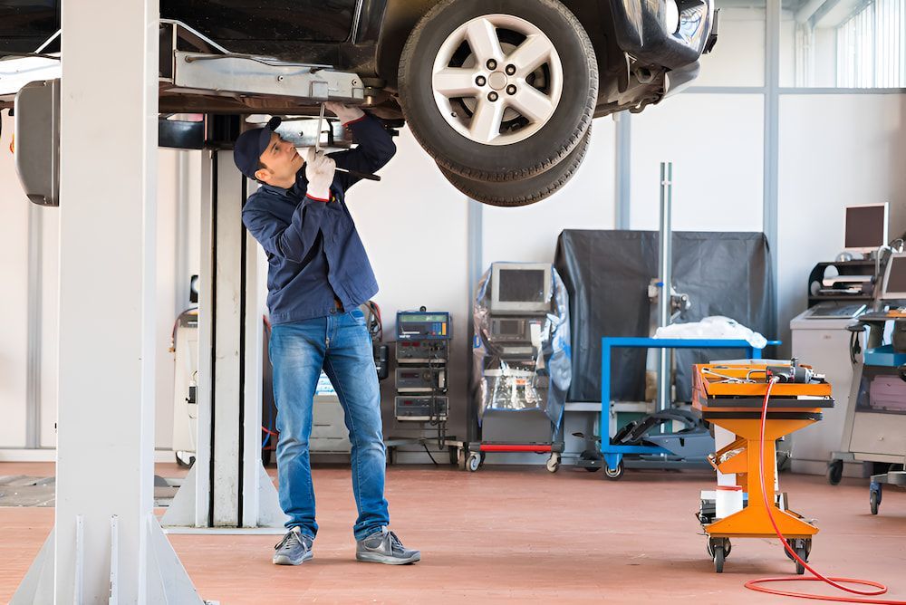 A Man Is Working On A Car On A Lift In A Garage β 100% Automotive In South Nowra, NSW