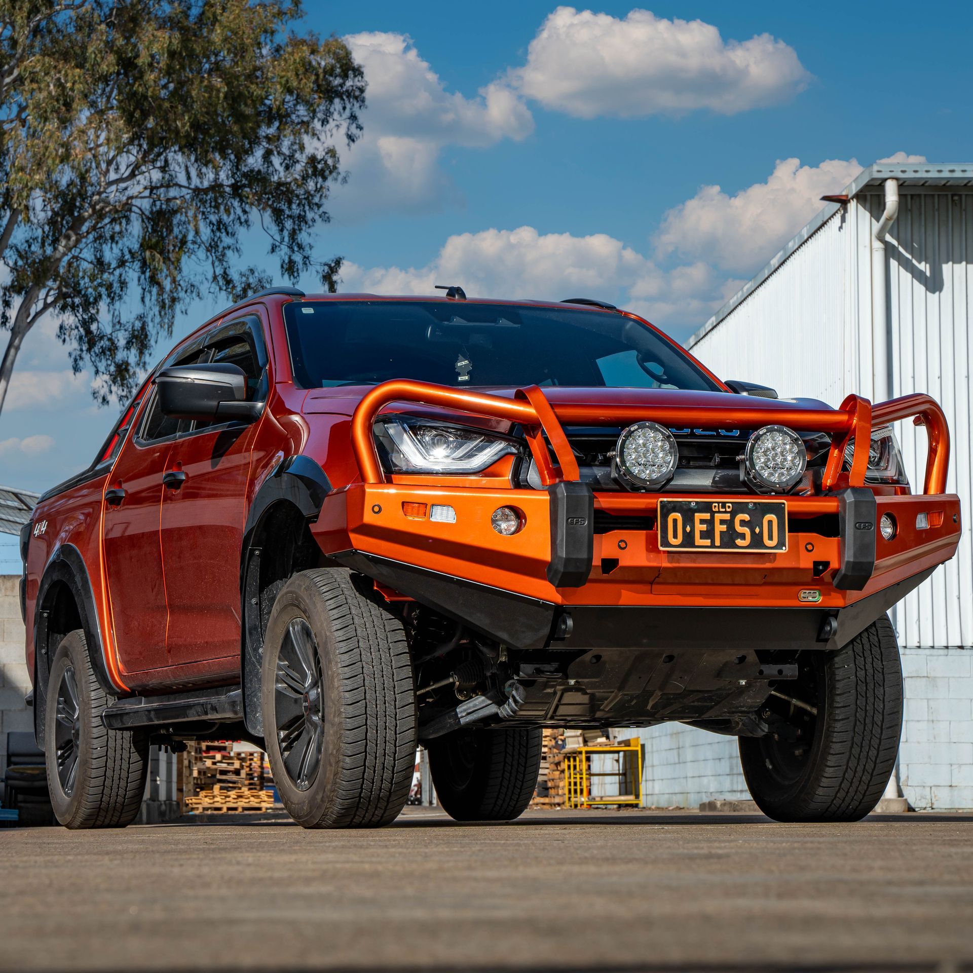Orange off-road pickup truck with black wheels and a protective bumper parked outdoors under a blue sky. — 100% Automotive In South Nowra, NSW