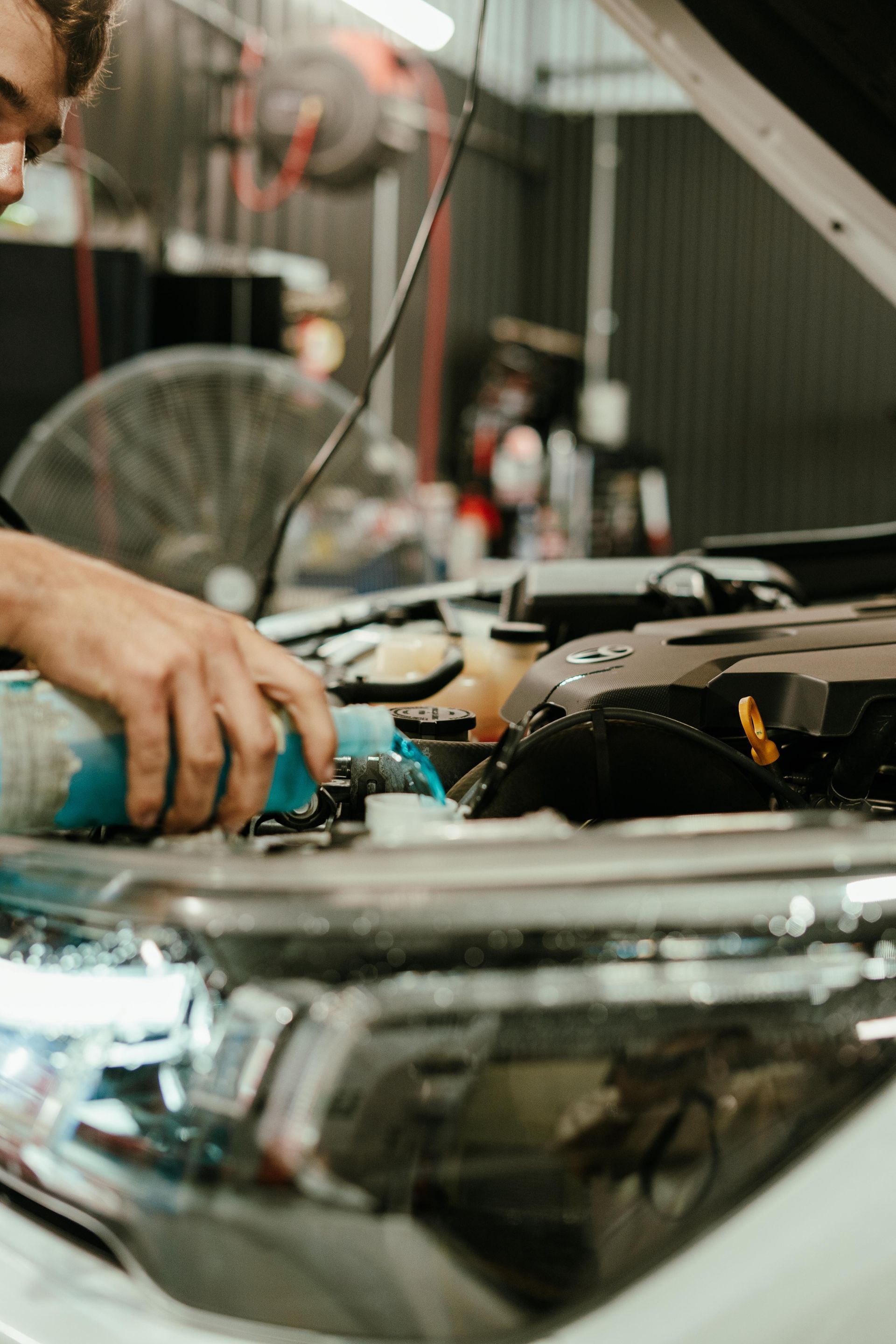 Mechanic working on a car engine in a garage; he is pouring liquid into the engine. — 100% Automotive In South Nowra, NSW
