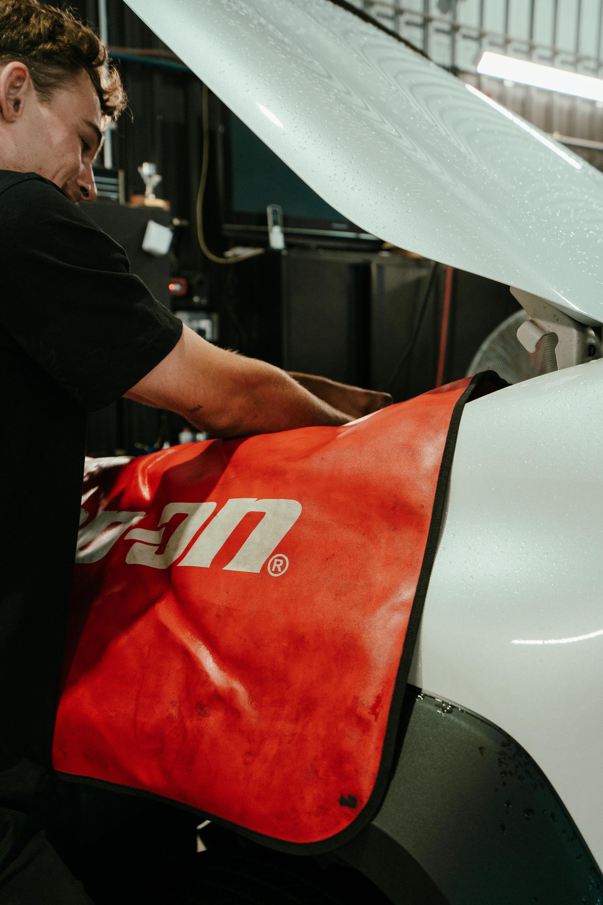 Mechanic working on a car engine with a red Snap-on fender cover. — 100% Automotive In South Nowra, NSW