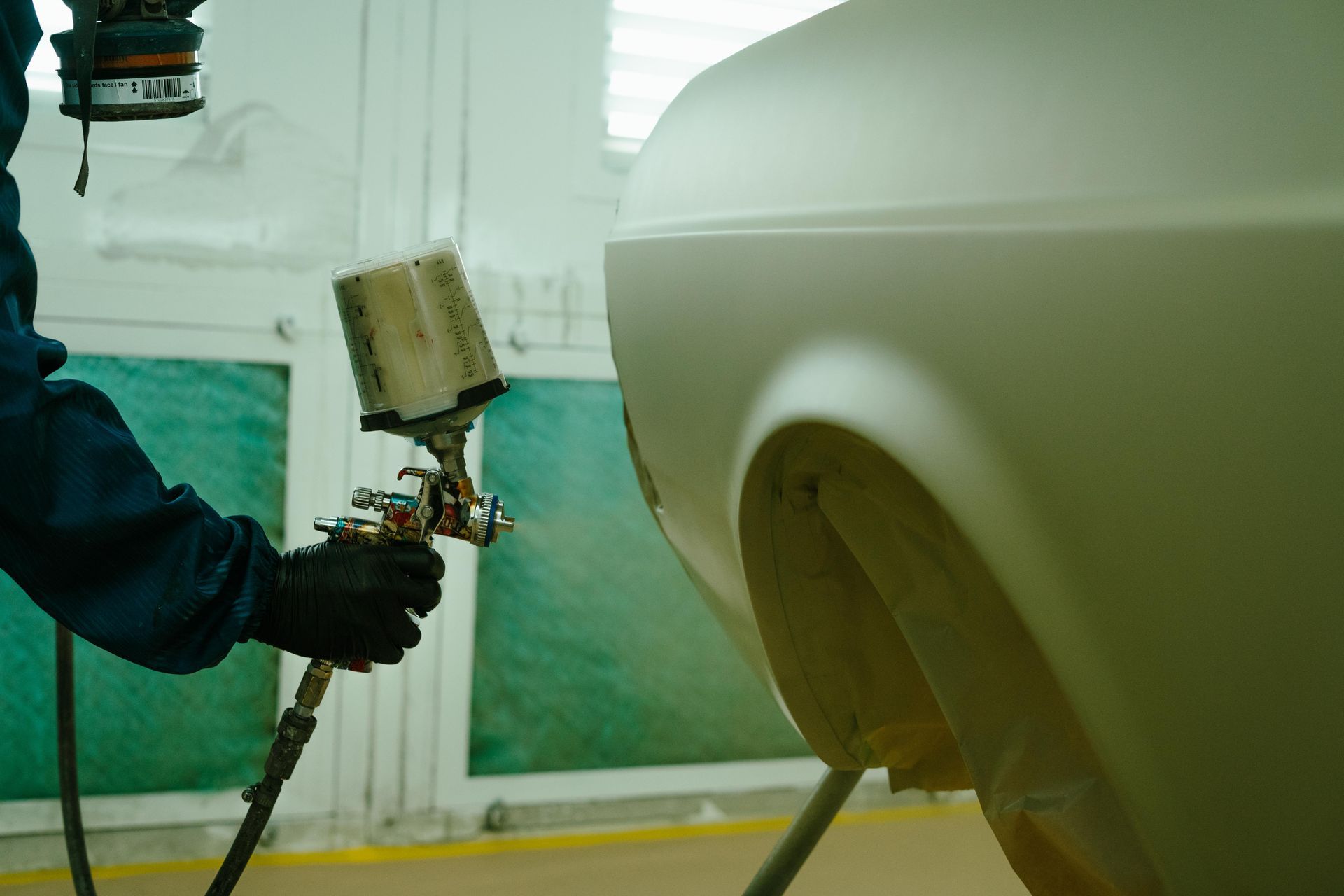 Person spray painting car fender with paint gun in a paint booth. — 100% Automotive In South Nowra, NSW