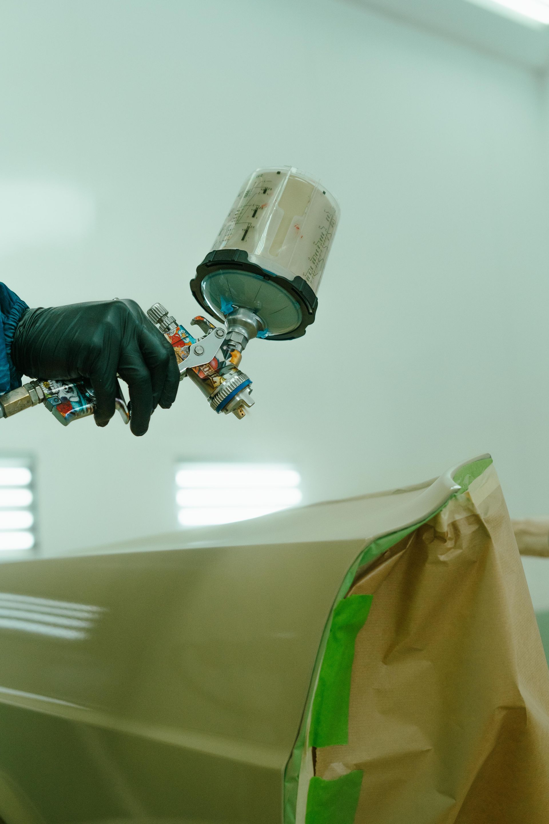 Person with black gloves using a paint sprayer on a car door in a paint booth. — 100% Automotive In South Nowra, NSW