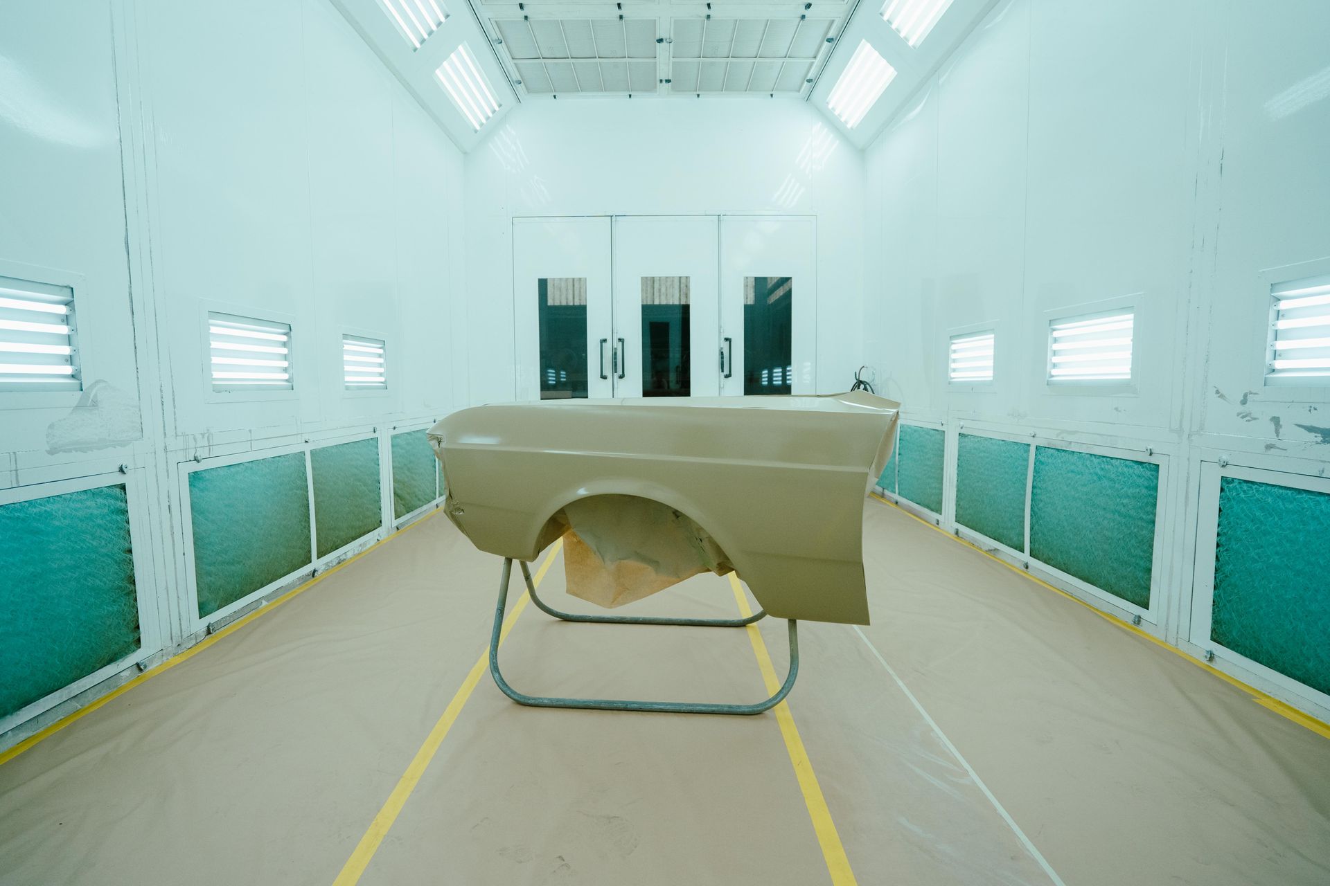 A car fender, painted beige, in a well-lit paint booth. — 100% Automotive In South Nowra, NSW