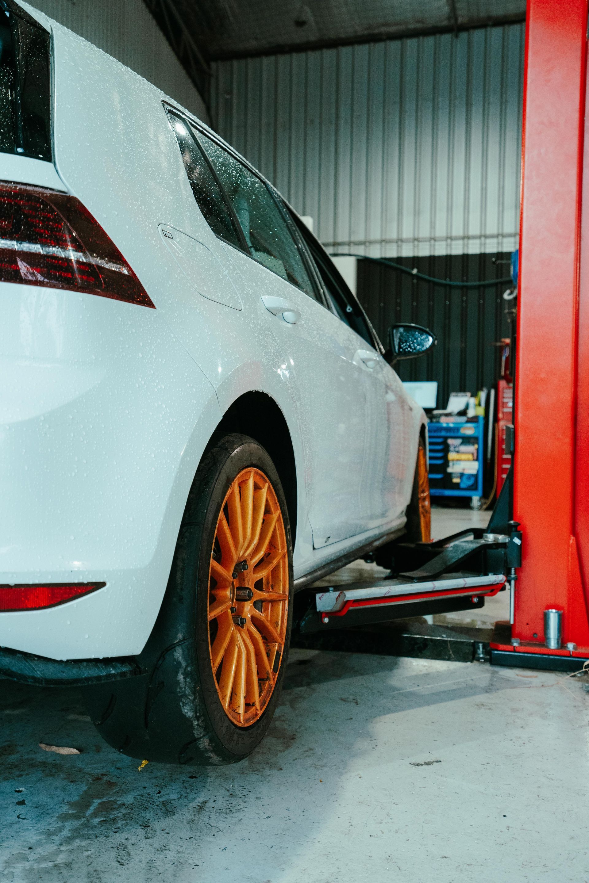 White car with orange wheels on a lift in a garage. — 100% Automotive In South Nowra, NSW