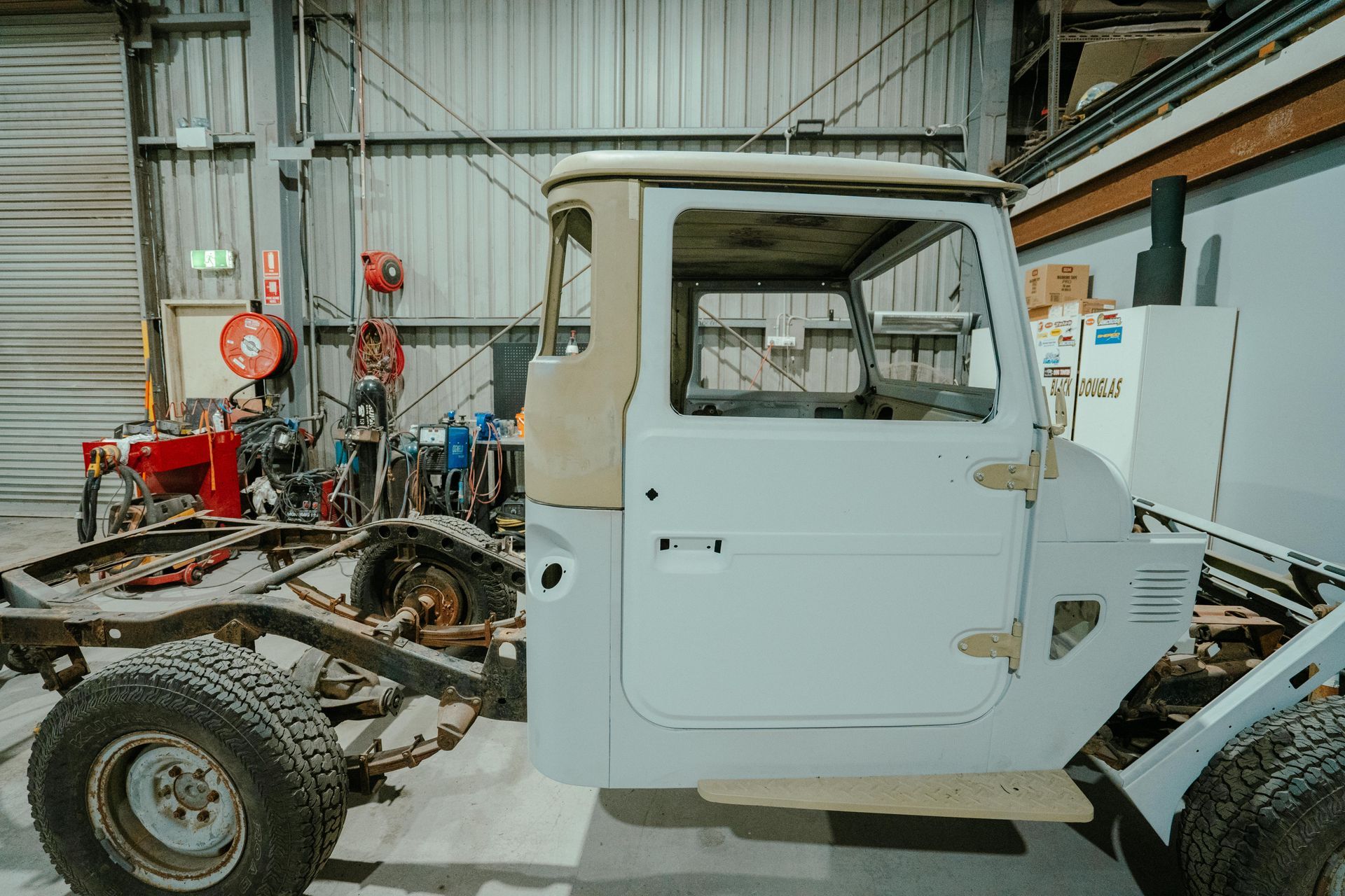 Partially restored vintage white Toyota Land Cruiser in a workshop; chassis visible. — 100% Automotive In South Nowra, NSW
