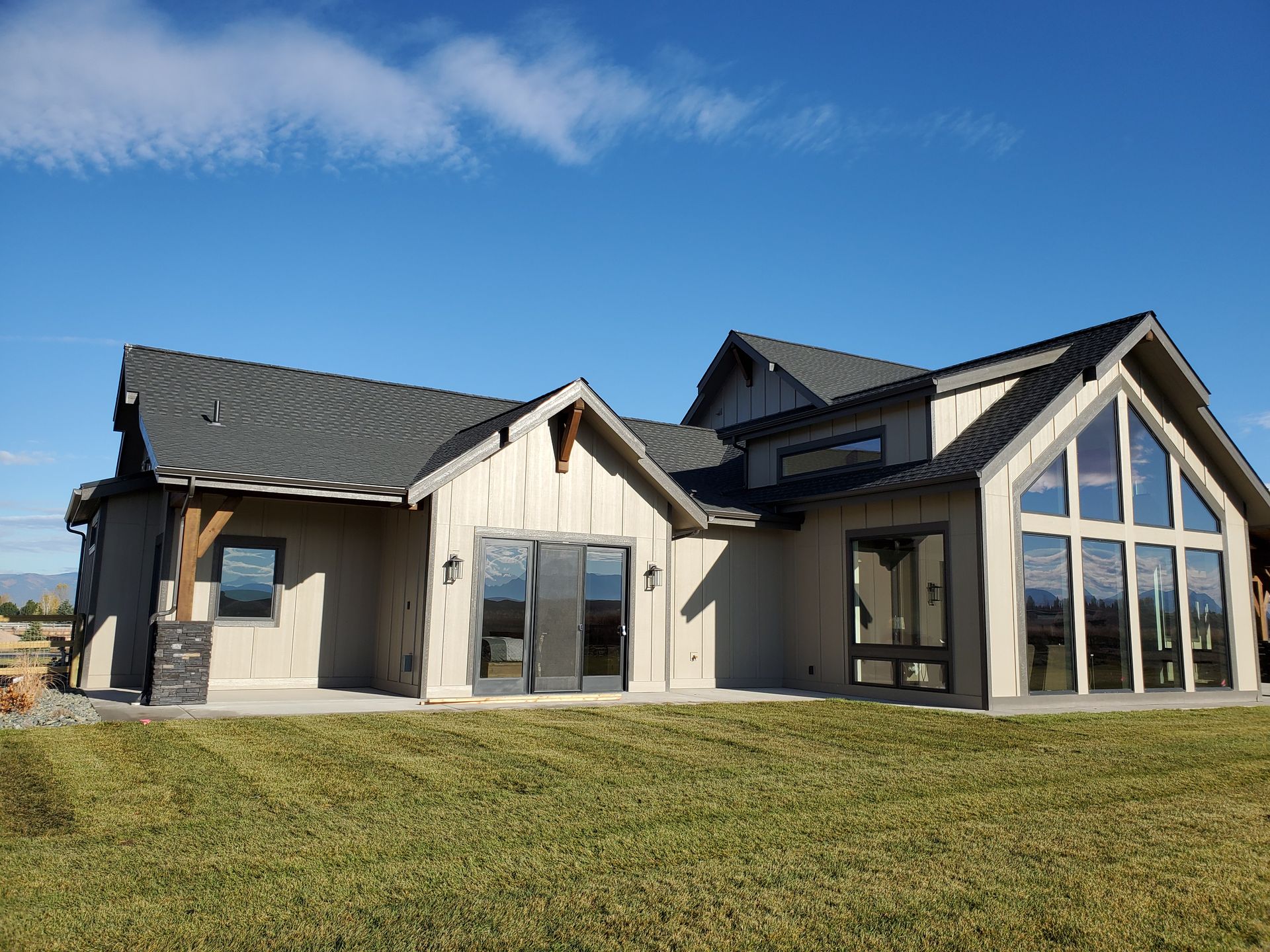 Modern beige barn-style building with dark roof and large garage doors on a gravel lot under a blue sky