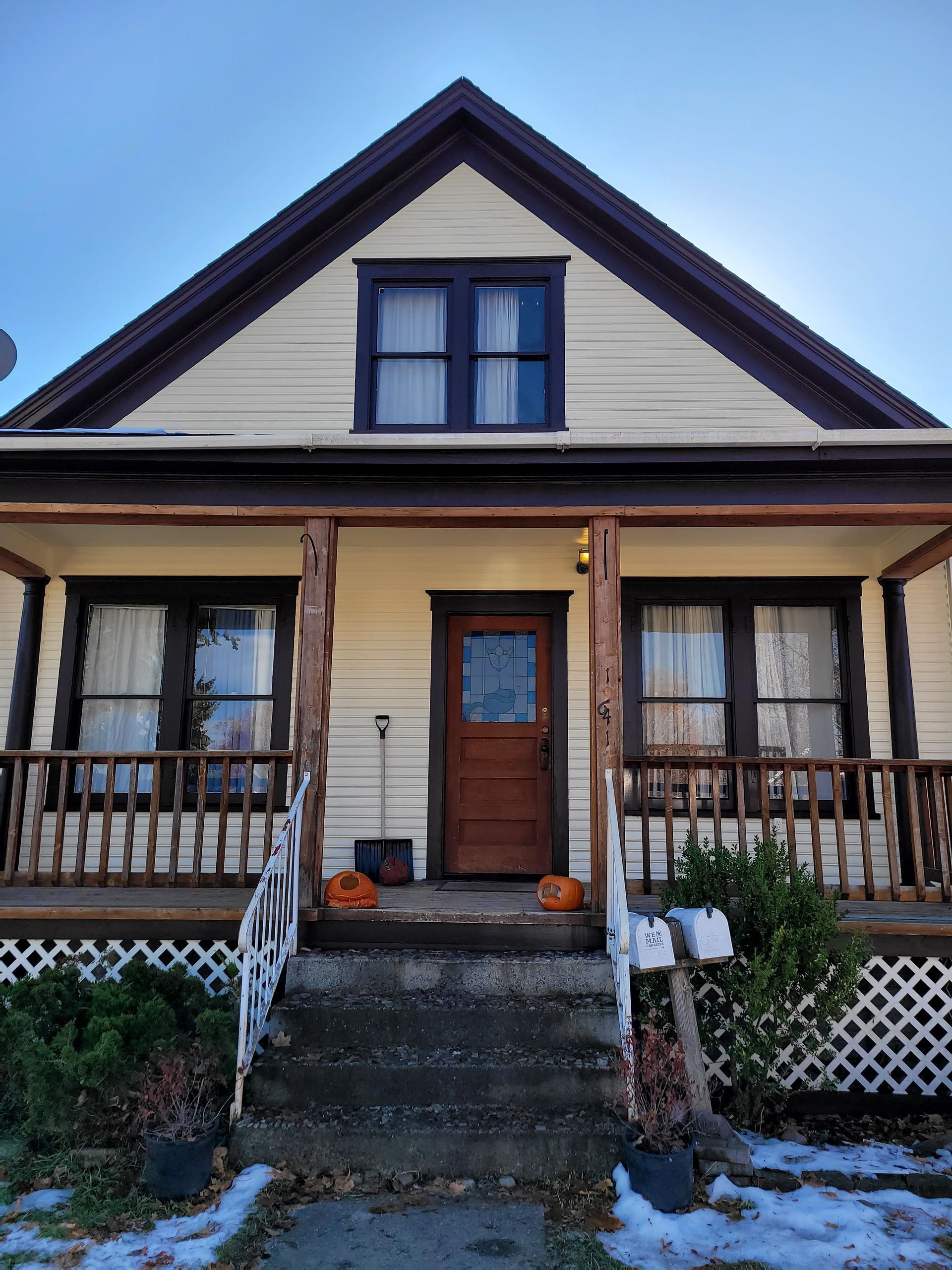 Front view of a beige house with dark trim, a front porch, steps, and a small pumpkin by the door