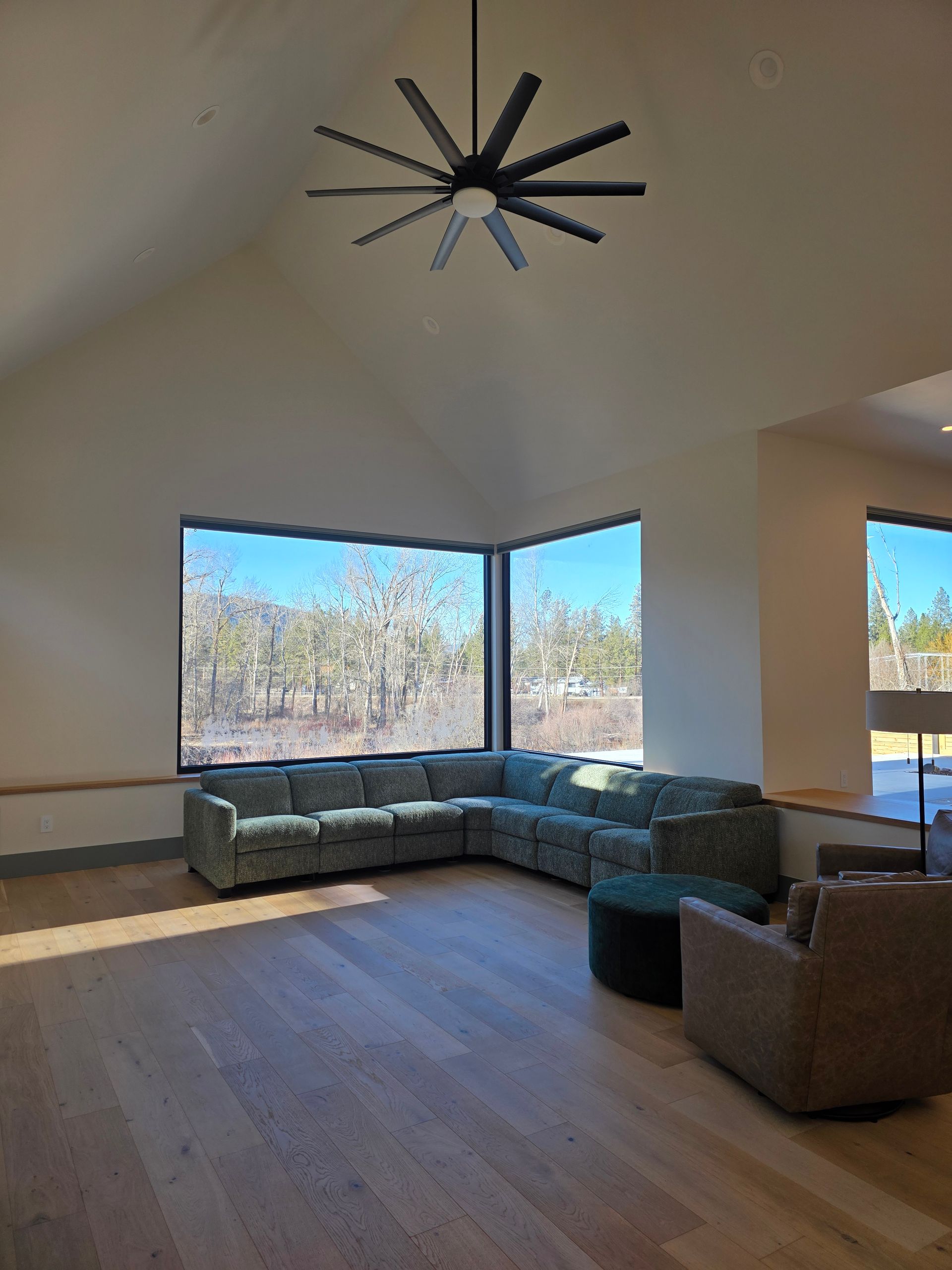 Bright living room with sectional sofa, armchairs, large windows, and a modern ceiling fan