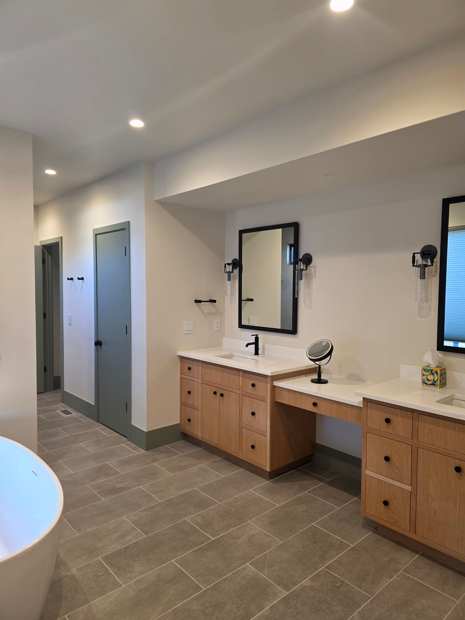 Public restroom with double sinks, mirrors, stall doors, and gray tile flooring.