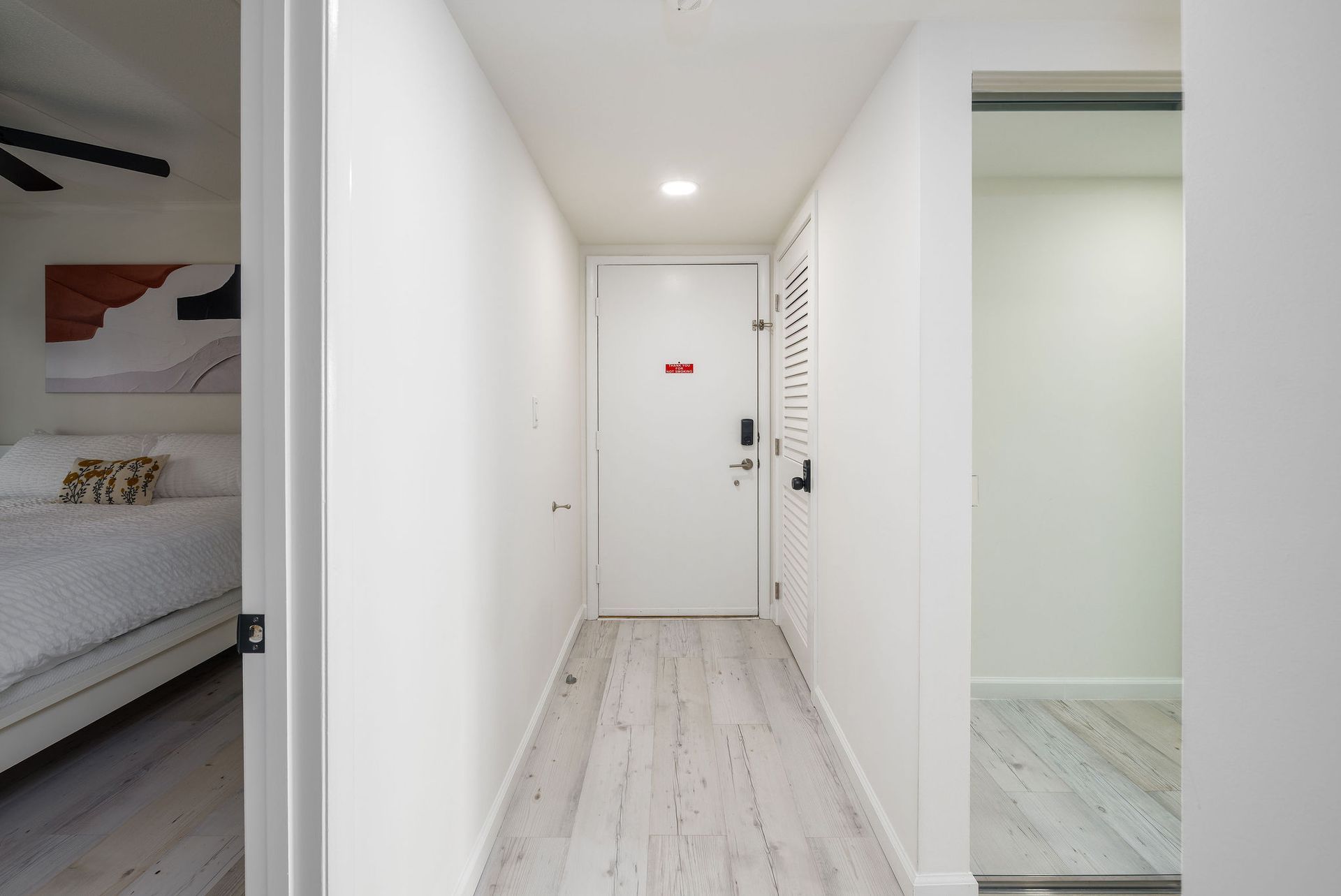 A long hallway with a white door and wooden floor leading to a bedroom.
