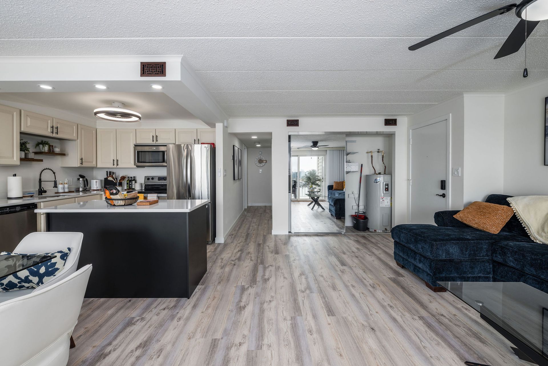 A living room filled with furniture and a kitchen with a ceiling fan.
