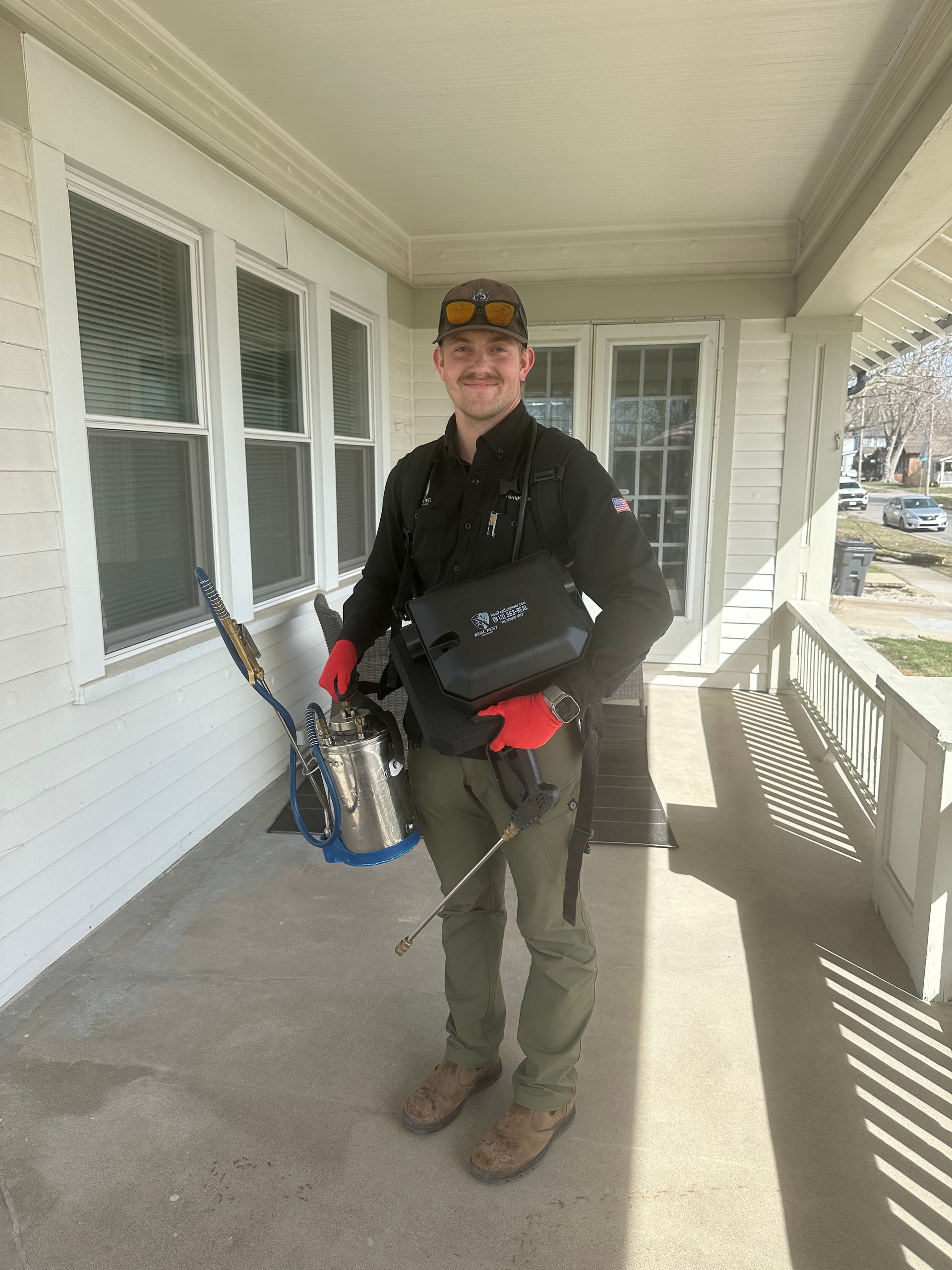 A real raccoon sits in a wire cage in front of a turquoise pest control truck featuring a cartoon raccoon decal.