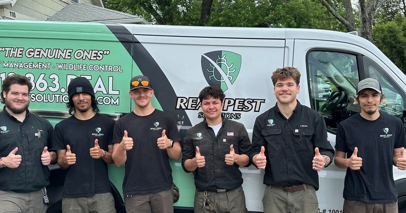 Six people in branded shirts standing in front of a Restapest van, all giving a thumbs-up gesture.
