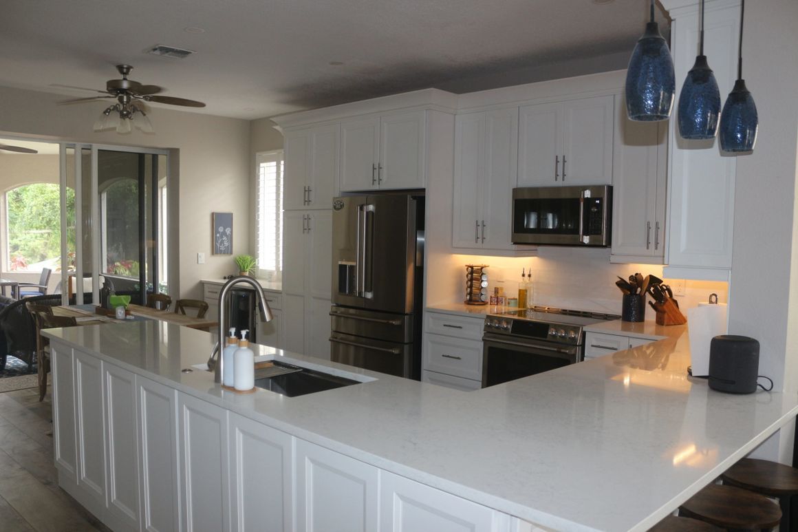 A kitchen with white cabinets , stainless steel appliances and a large island.