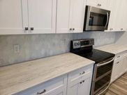 A kitchen with white cabinets , a stove , microwave and oven.