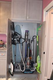 A laundry room with a vacuum cleaner , ironing board and mop.