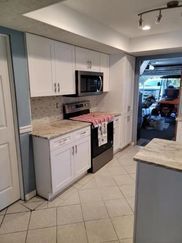 A kitchen with white cabinets , a stove and a microwave.