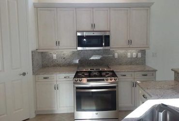 A kitchen with white cabinets , a stove , a microwave , and a sink.