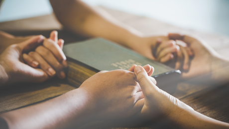 A couple of people are holding hands over a bible.