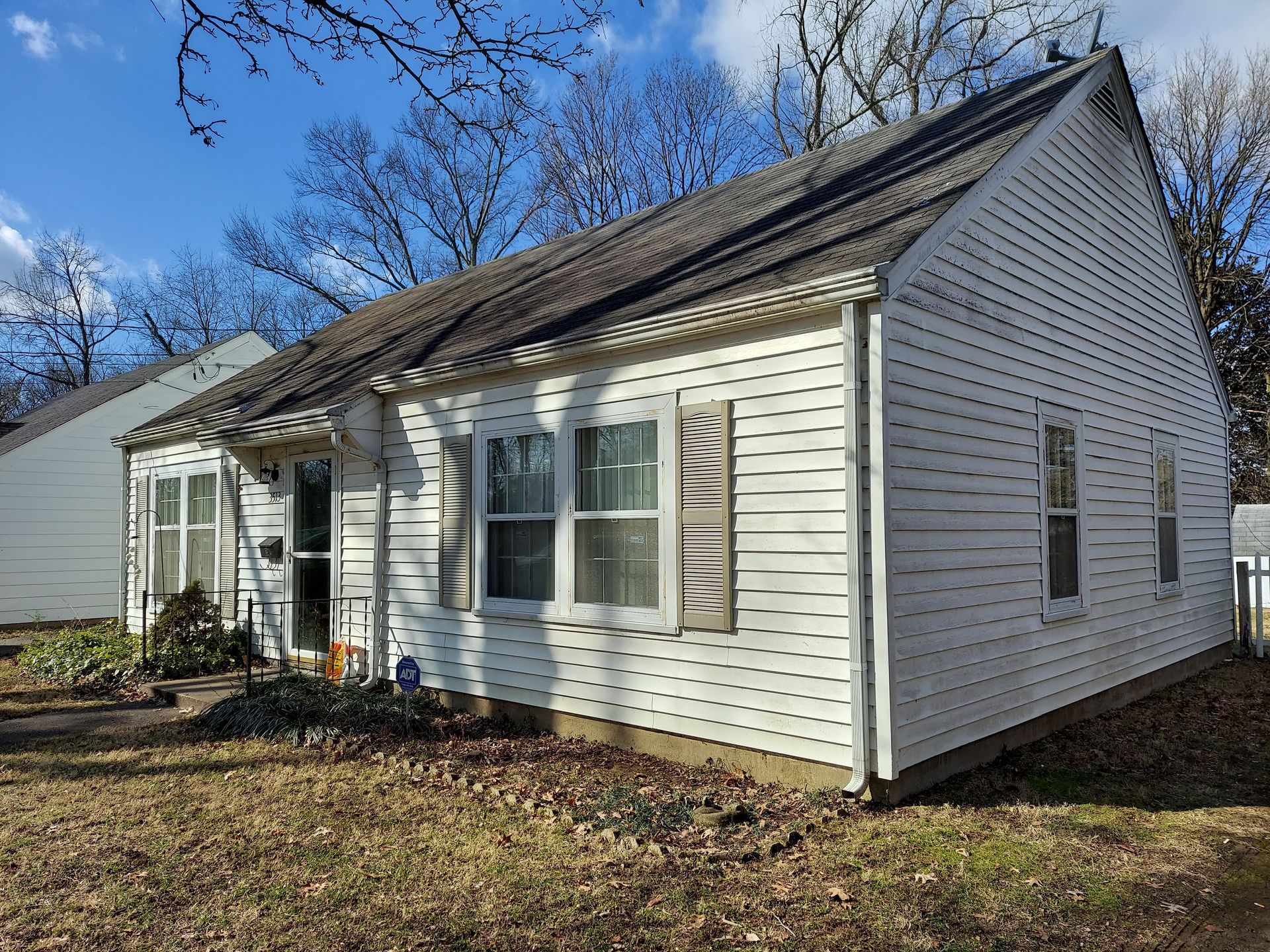 White, single-story house with a dark roof and brown yard, under a blue sky.
