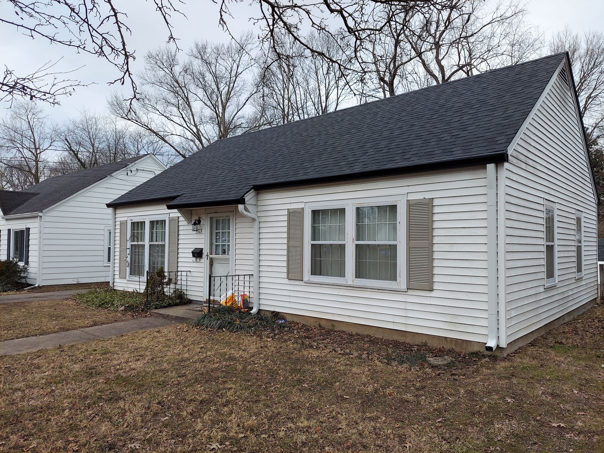 White house with black roof and beige shutters on a cloudy day.