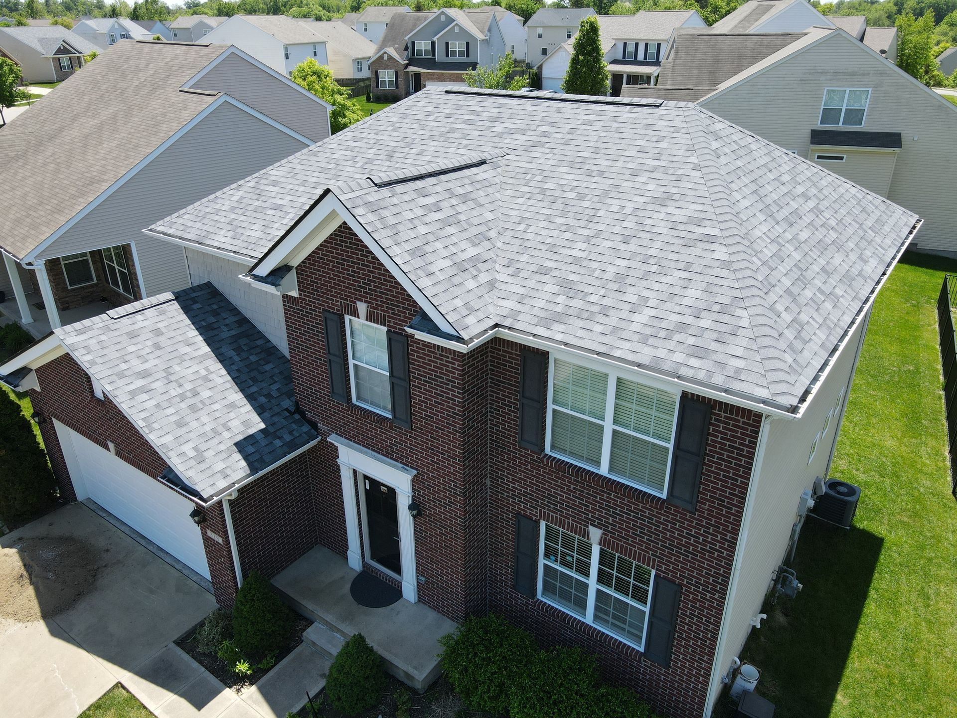 Aerial view of a two-story house with a gray roof and brick facade in a residential neighborhood.