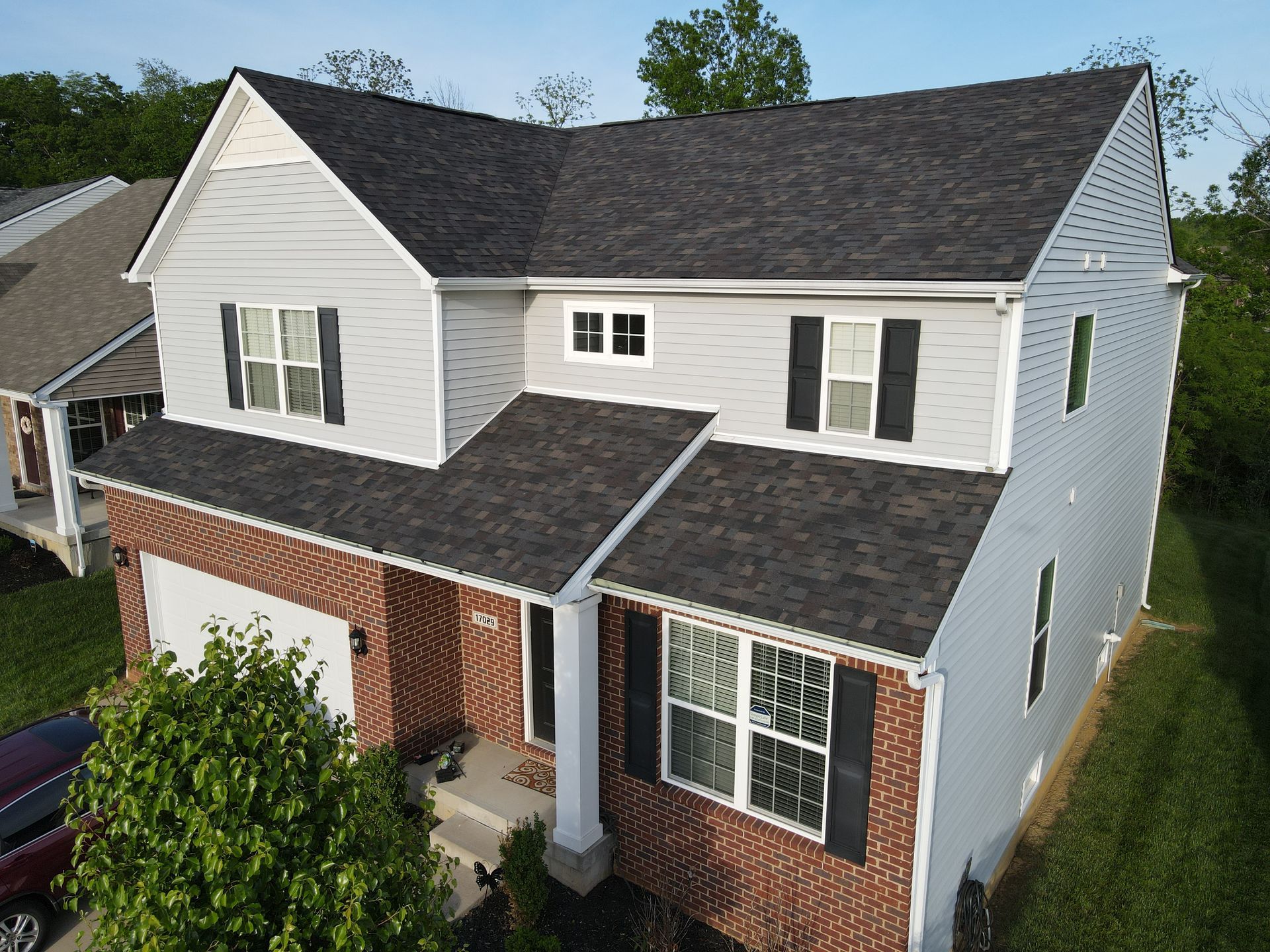 Two-story house with gray siding, brick facade, and dark roof.