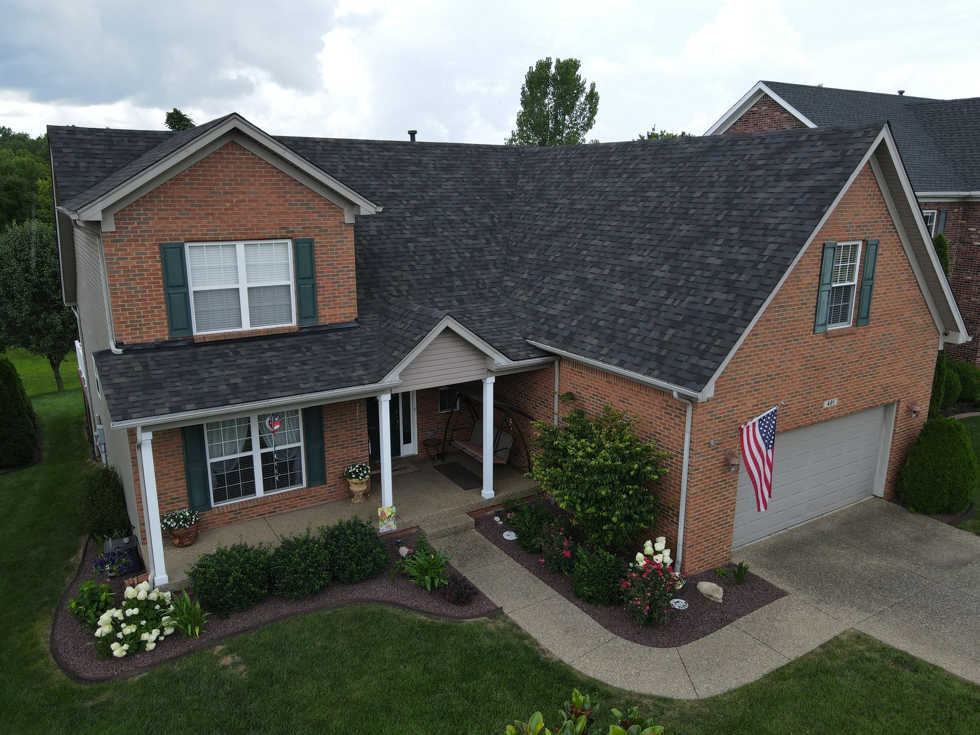 Brick house with dark roof, front porch, and American flag hanging.