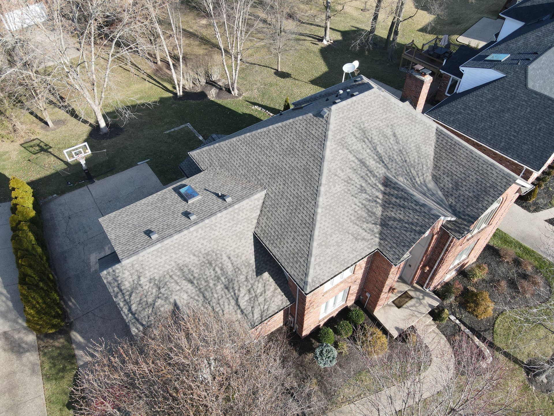 Aerial view of a gray-roofed brick house with a driveway and surrounding trees.