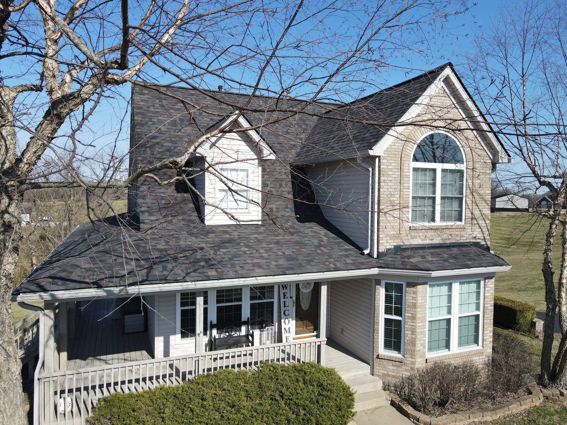 Two-story brick house with dark roof and white trim, front porch, and dormers under a blue sky.