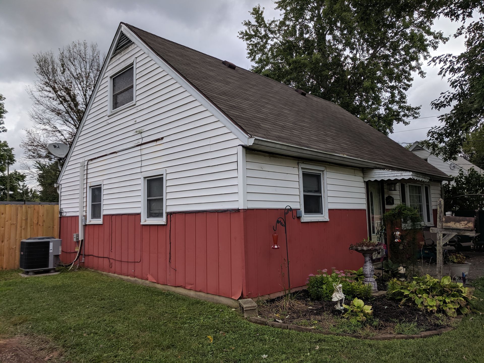 Two-story house with red siding on the bottom and white on the top; dark brown roof; cloudy sky.
