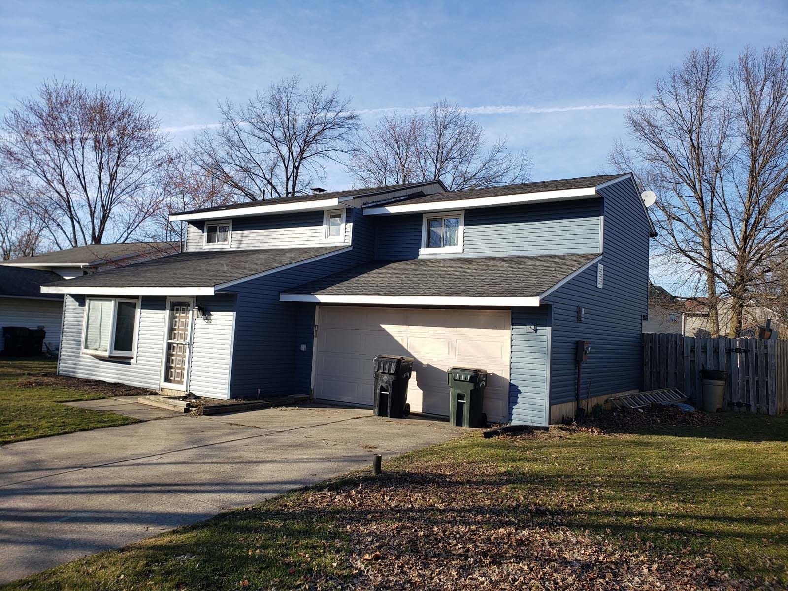 A house with a driveway and trash cans in front of it.