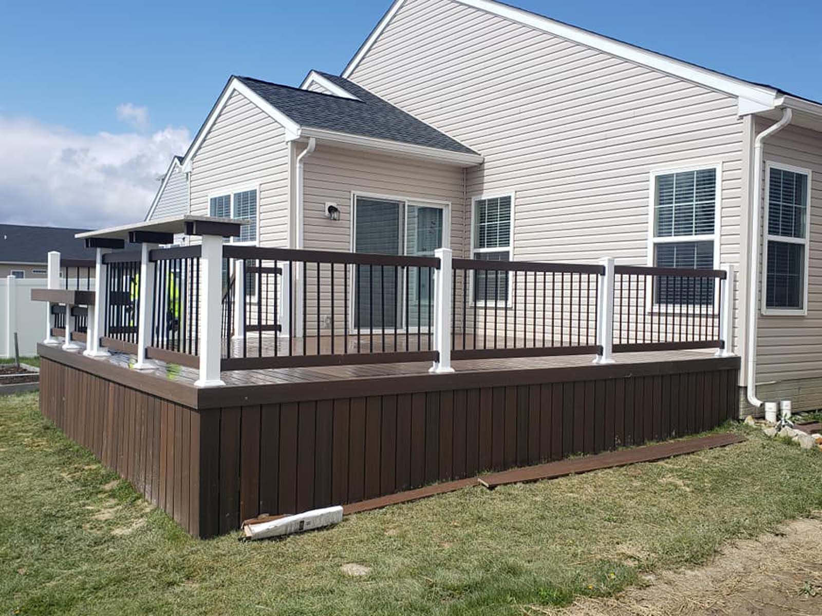 A large deck with a railing is in front of a house.