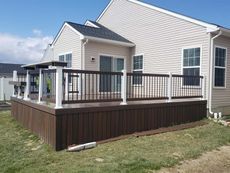 A large deck with a railing is in front of a house.