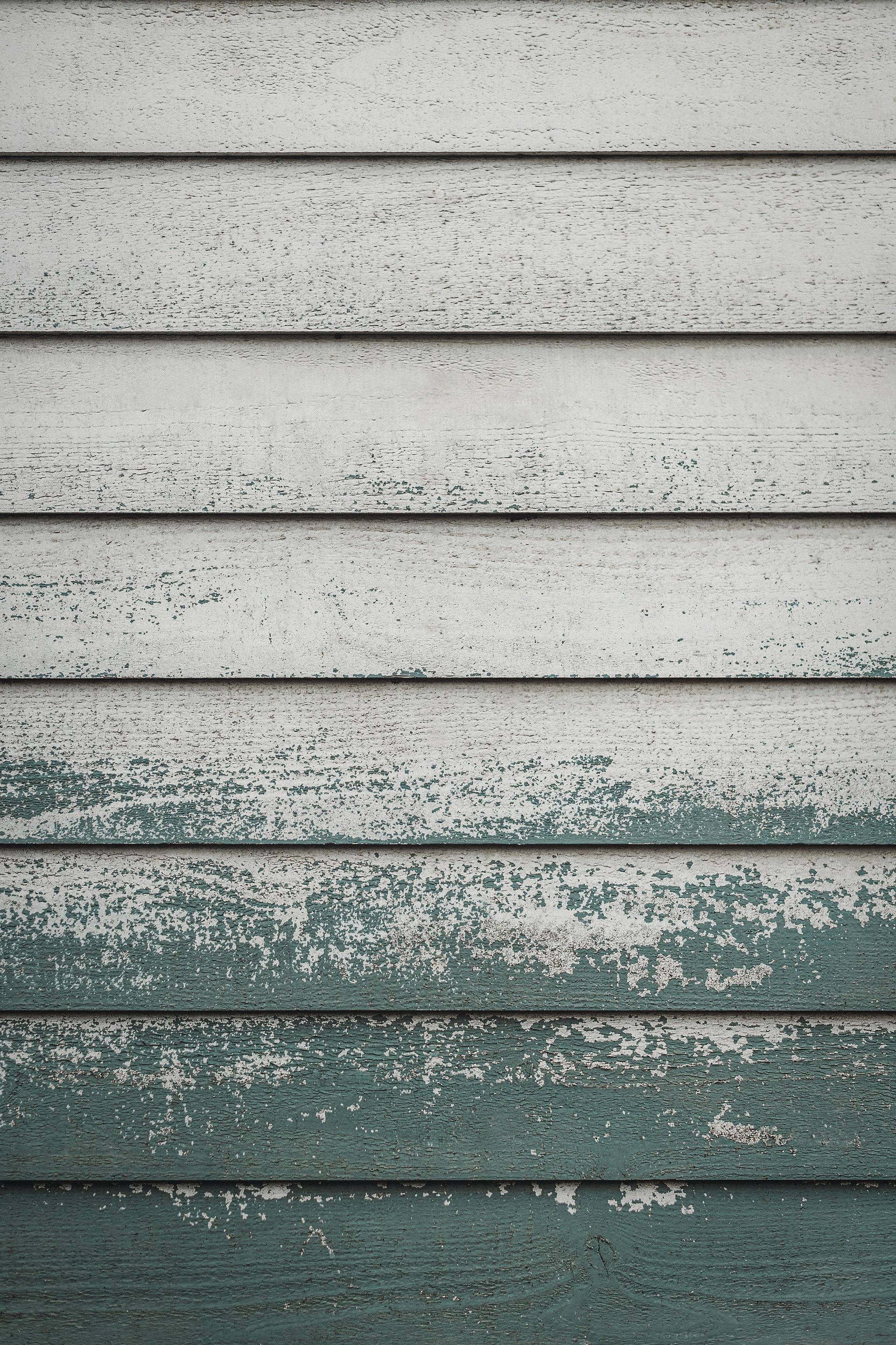 Weathered horizontal siding with peeling pale paint and a darker green lower section