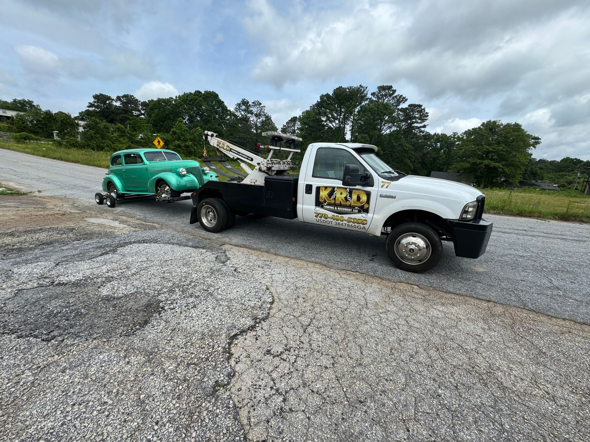 A tow truck is towing a green car down a road.