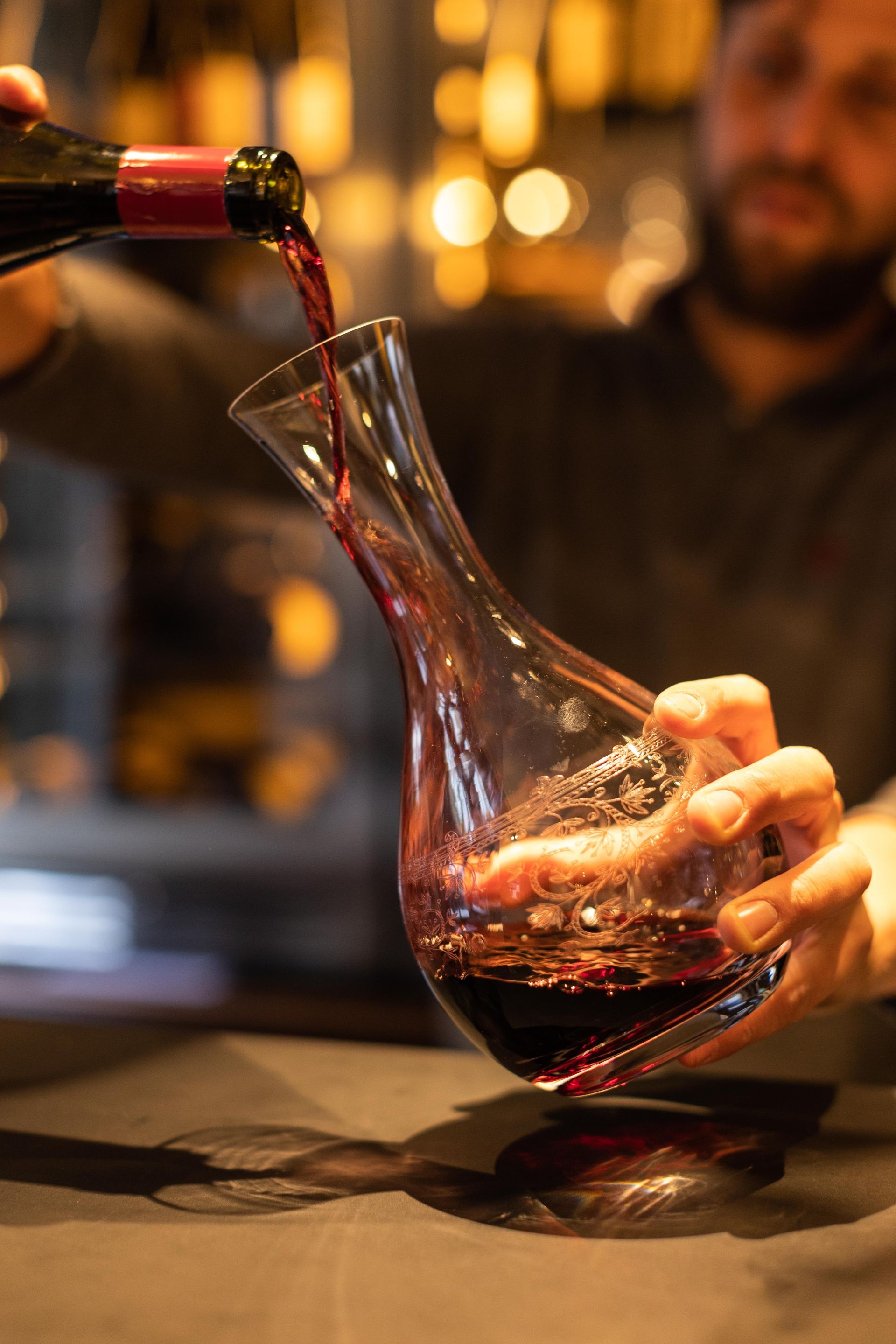 Un homme verse du vin rouge dans une carafe en verre.