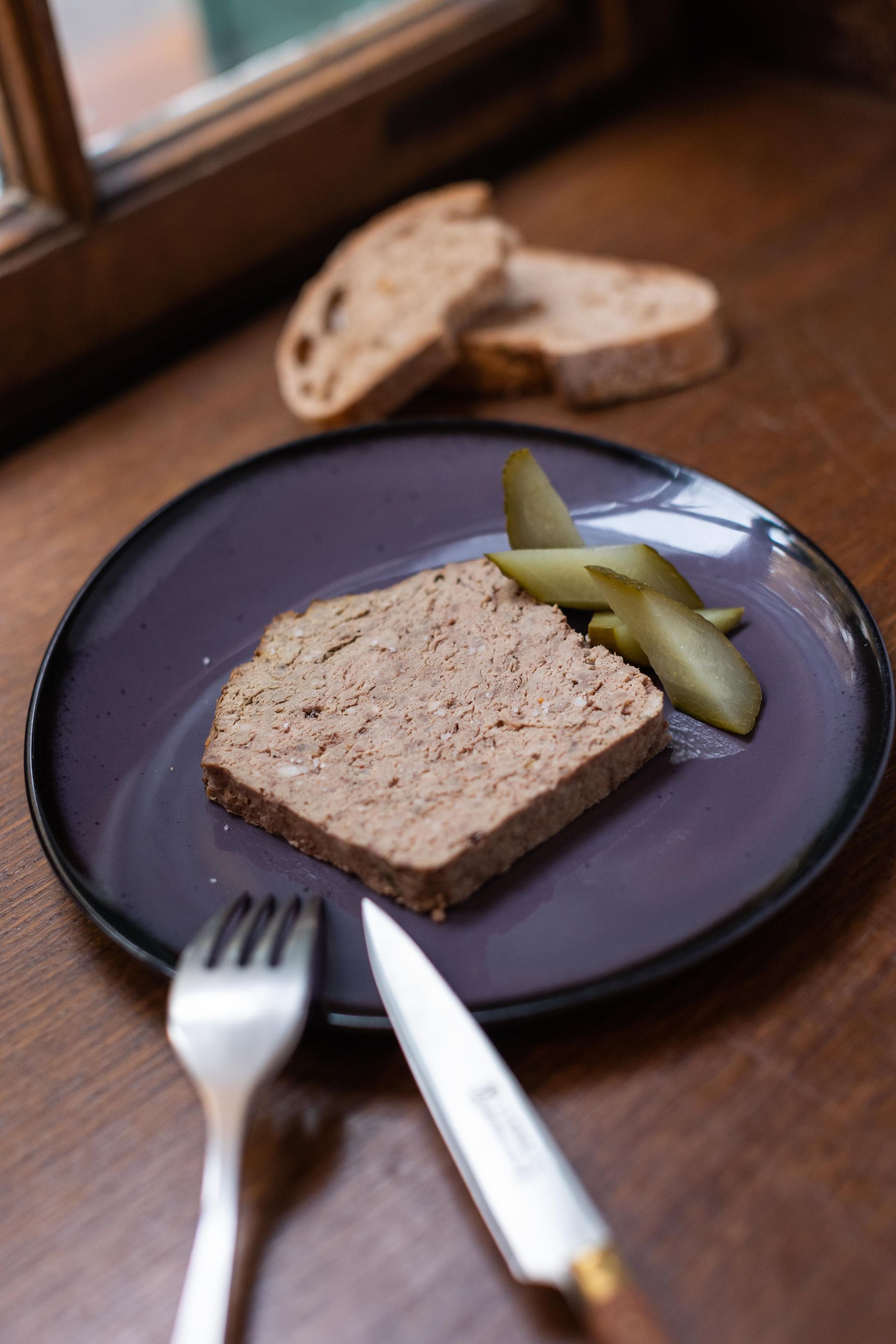 Une assiette violette avec un morceau de viande et des cornichons dessus
