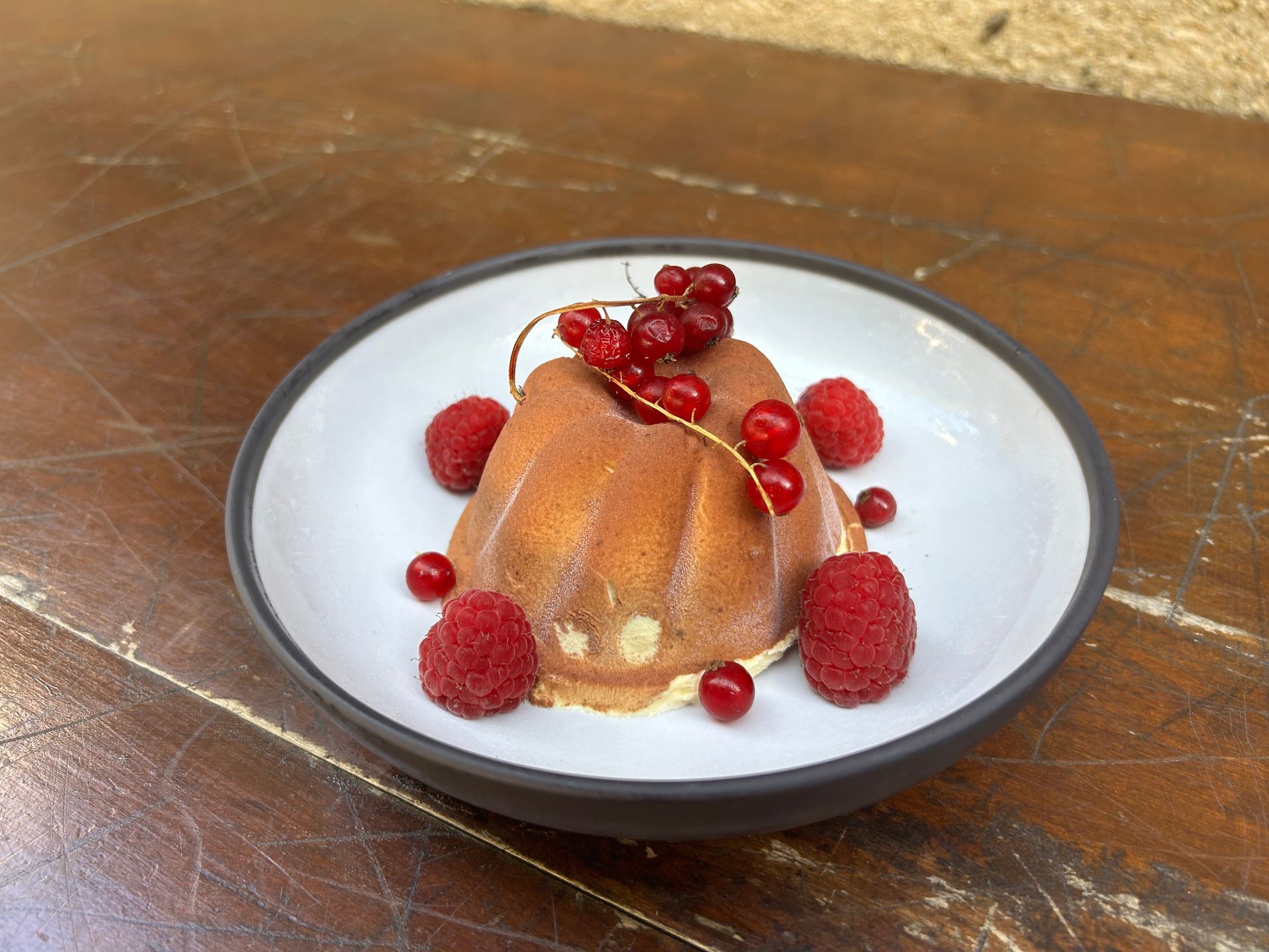 Une assiette blanche garnie d'un dessert et de framboises sur une table en bois.