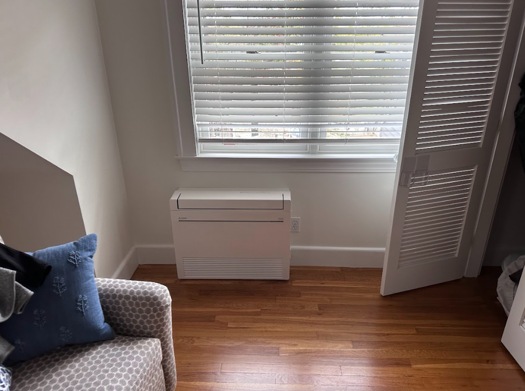 Room with window, blinds, white heater, wood floor, open white shutter, and a patterned armchair.