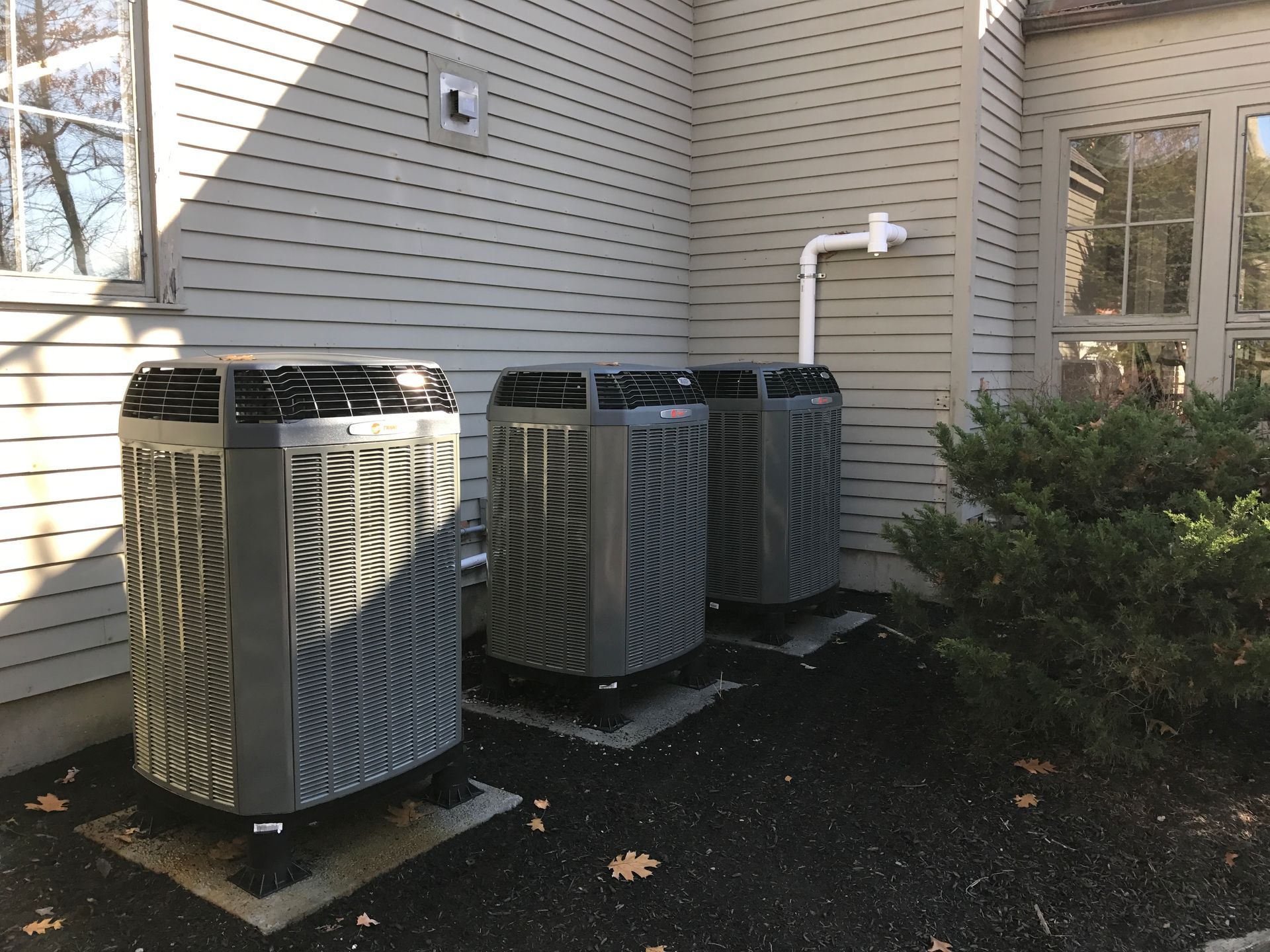 Three heat pumps are sitting on the side of a building.