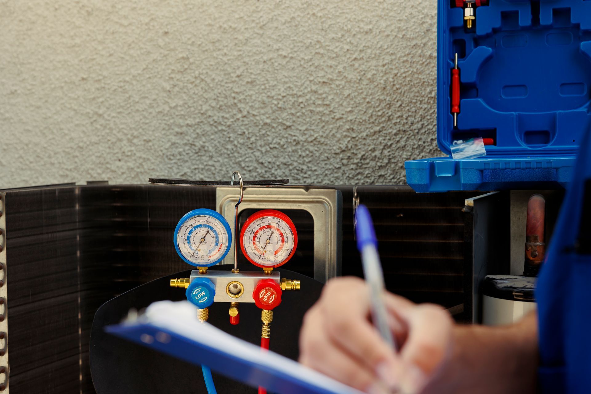 HVAC technician checking gauges on cooling unit, writing on a clipboard.