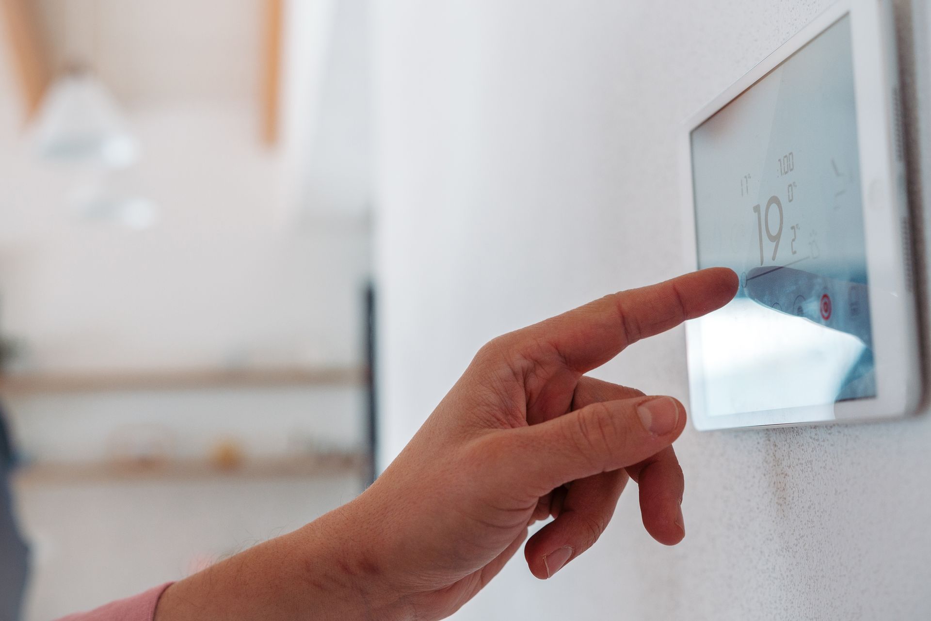 Hand adjusting a digital thermostat on a white wall, setting the temperature.