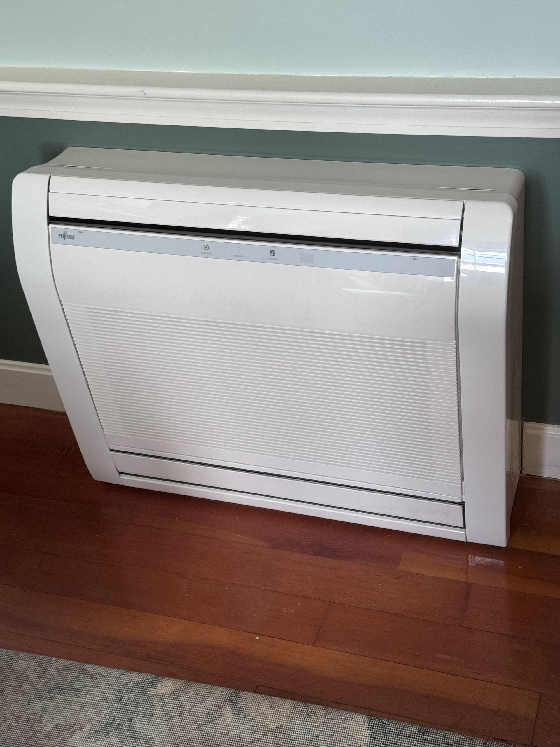 A white air conditioner is sitting on a wooden floor in a living room.