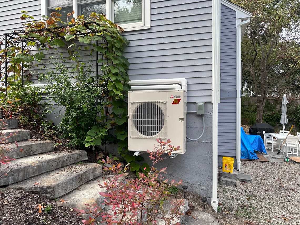 A white air conditioner is mounted on the side of a house.