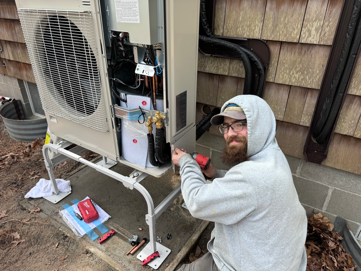 A man in a hoodie is working on an air conditioner.