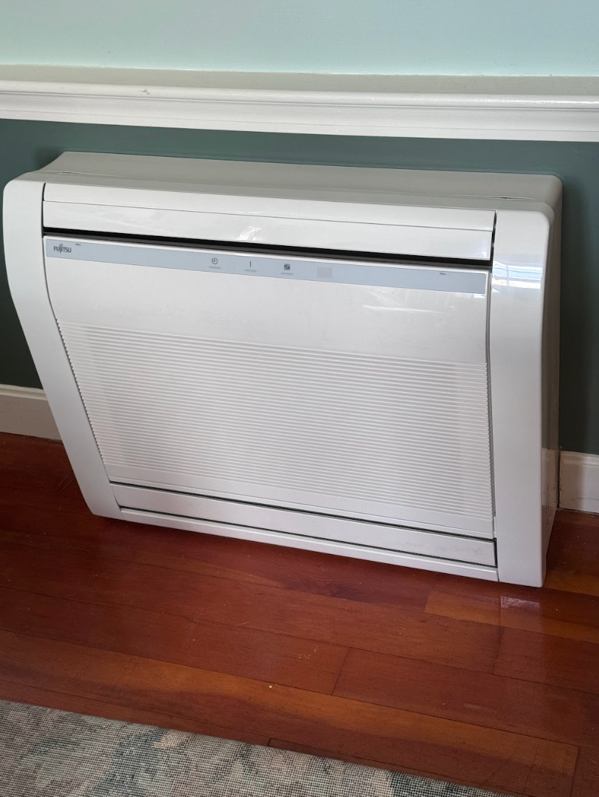 A white air conditioner is sitting on a wooden floor next to a wall.