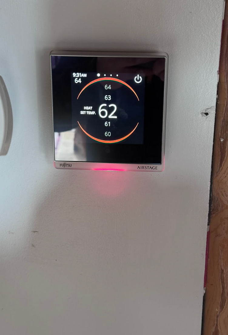 A thermostat on a white wall shows that the temperature is 62 degrees