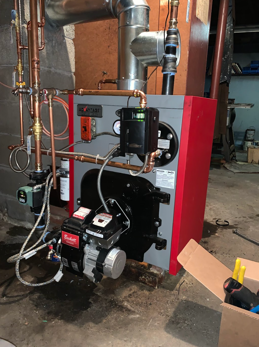 A red and gray boiler is sitting in a basement next to a box.