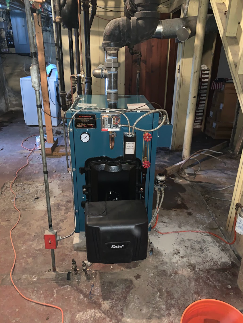 A blue boiler is sitting in a basement next to a staircase.